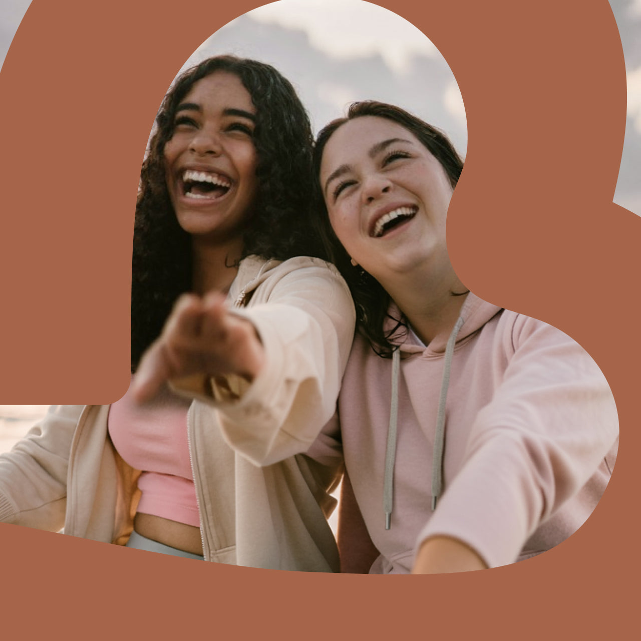 Two people laughing joyfully while pointing at camera, framed within an orange rounded rectangular Bodywealth logo shape against a cloudy sky background. One person wears a beige cardigan over a pink top, the other wears a pink hoodie.